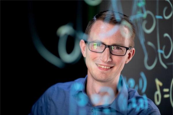 Zachery DeBruine in a blue shirt behind a screen with coding written on it