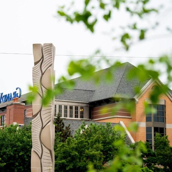 A tall carved sculpture is in the foreground, with a building and the word "Grand" visible in the background.