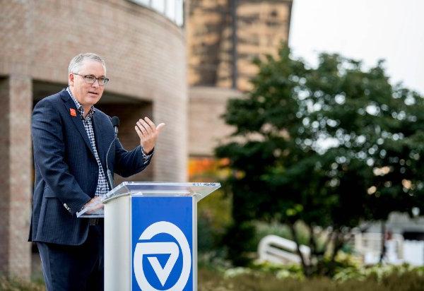 A person gestures with the hand while speaking at a podium with the Grand Valley logo.