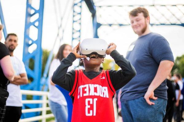 A person wearing a jersey that says "Rockets" and the number 13 looks through a VR headset. 一个人在背后微笑.