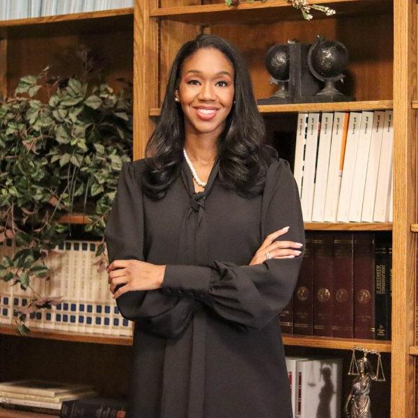 Kyra Harris Bolden stands with arms crossed in front of a bookcase