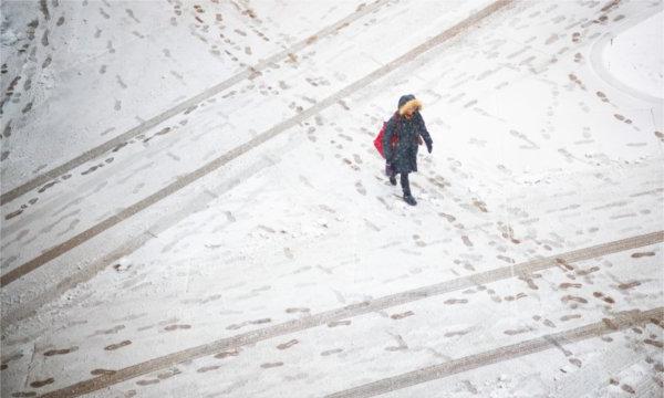  一个穿着冬衣的人走在积雪覆盖的人行道上. 