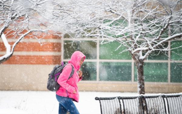  一名大学生用粉红色的兜帽罩住自己的头，让自己远离下雪的天气. 