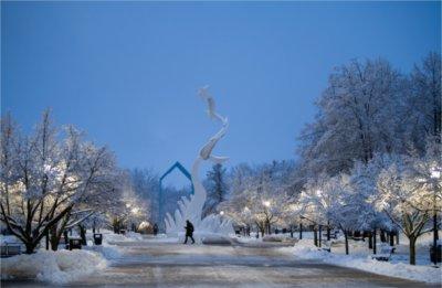 黎明时分，一个人走过下雪的大学校园里的一座雕塑.