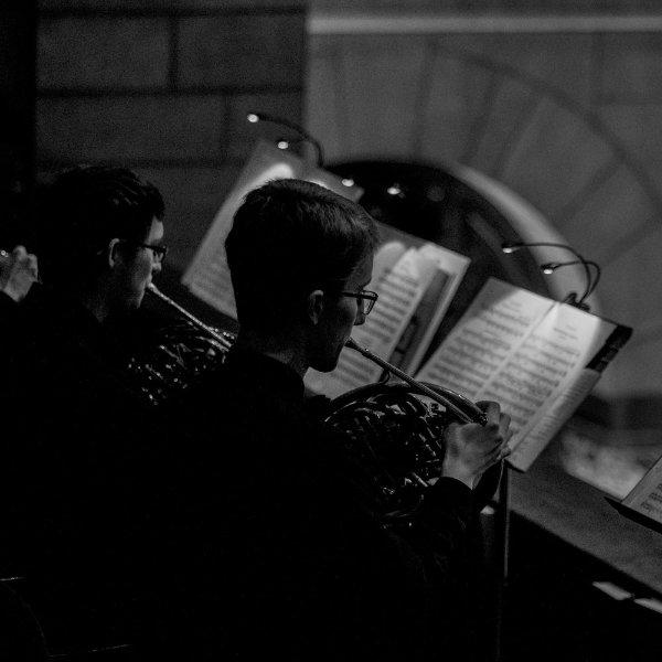 People are playing brass instruments in a balcony. Sheet music is in front of them.