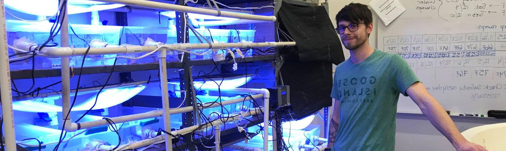 MS Biology Graduate Student Tyler Harman at the Annis Water 资源 Institute in Muskegon conducting research on cold-water corals and posing in front of custom recirculating aquarium system.